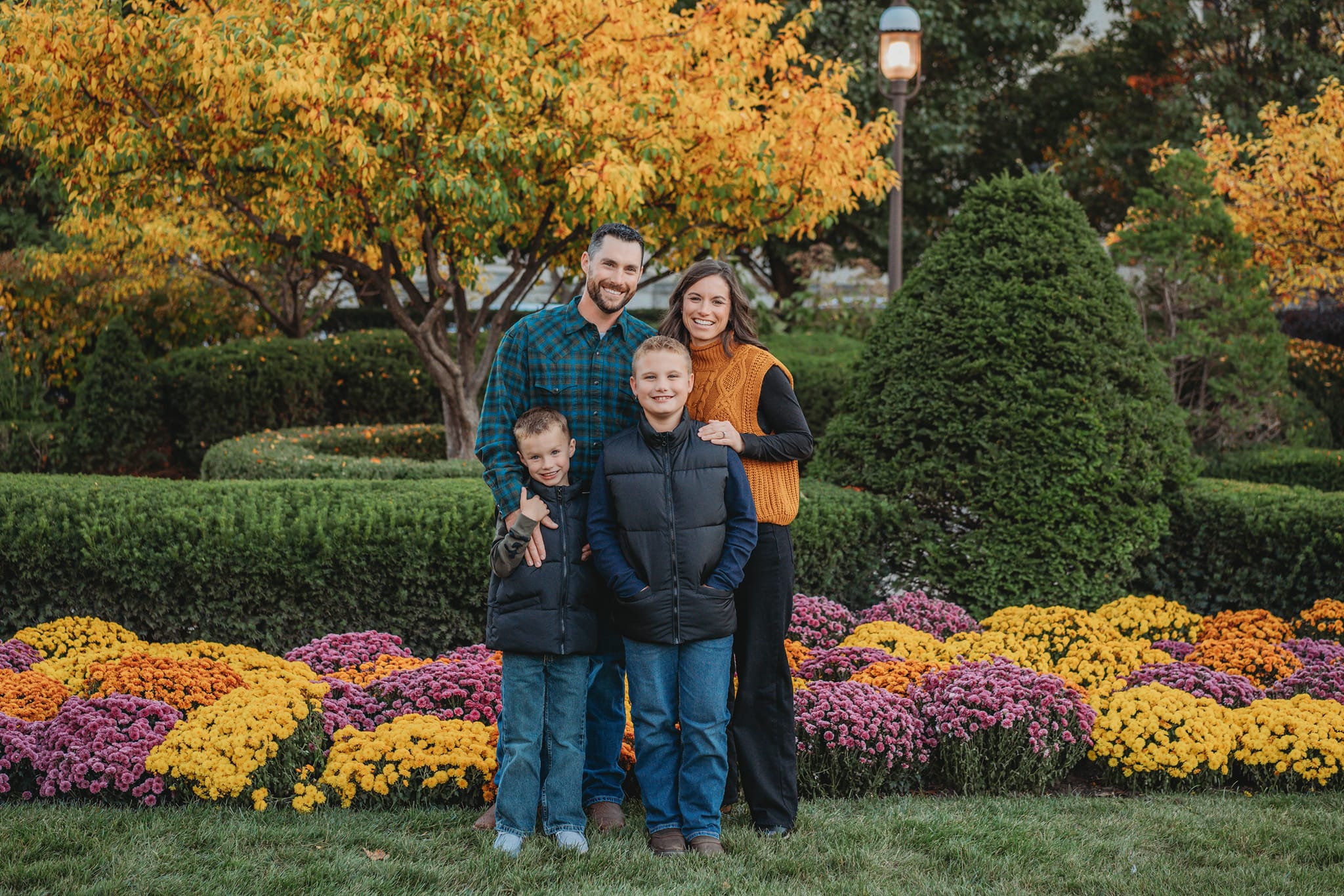 Family of four posing in a garden with autumn foliage and flowers.